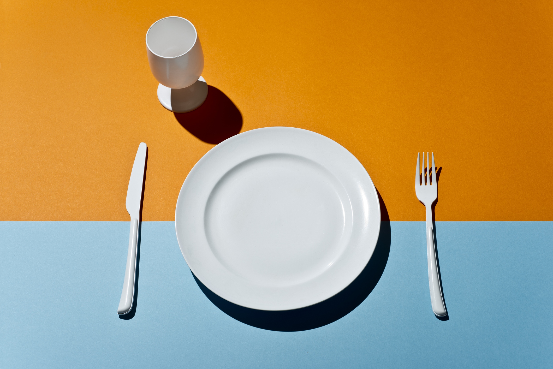 High Angle View Of white glass, fork, knife and plate on a colored table